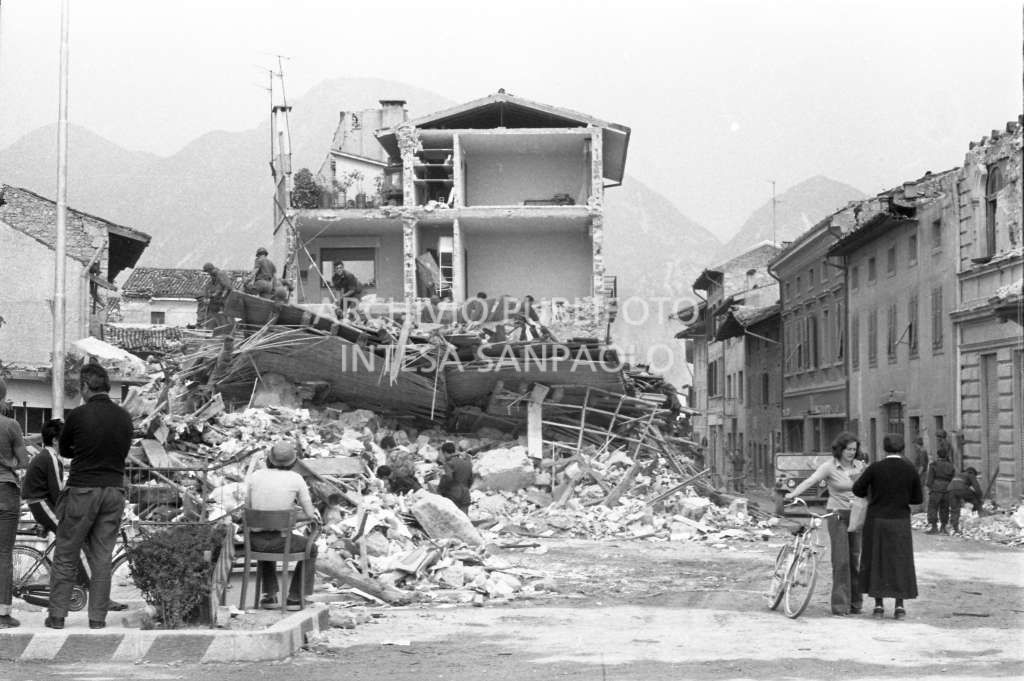 Alcuni passanti osservano gli edifici danneggiati dal terremoto in località del Friuli