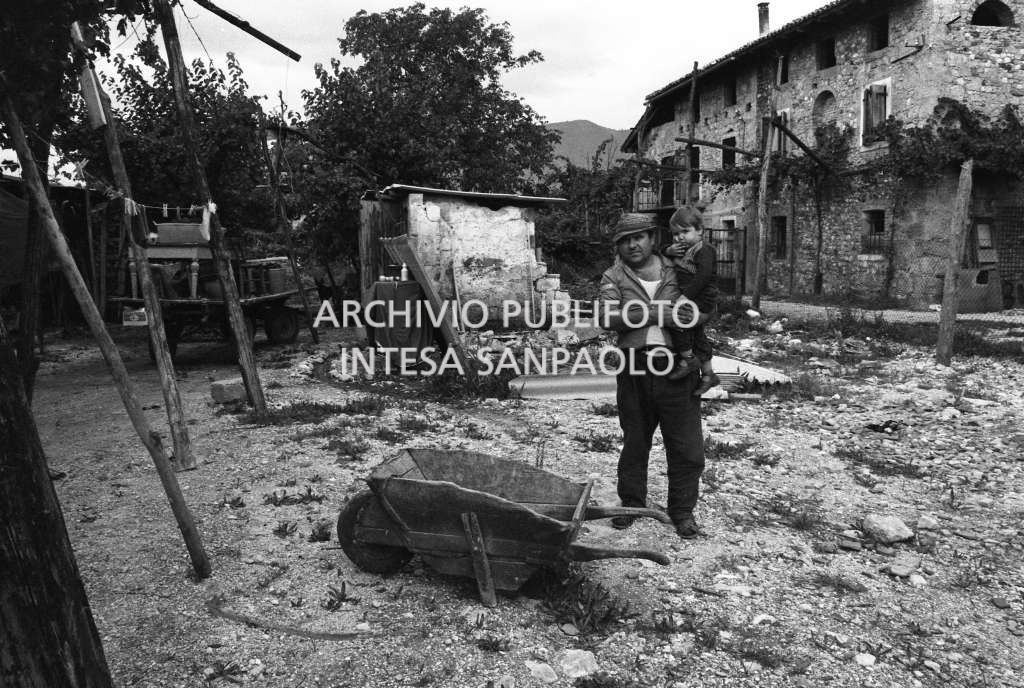 Un uomo ritratto con un bambino in un cortile, visibile alle loro spalle una cascina