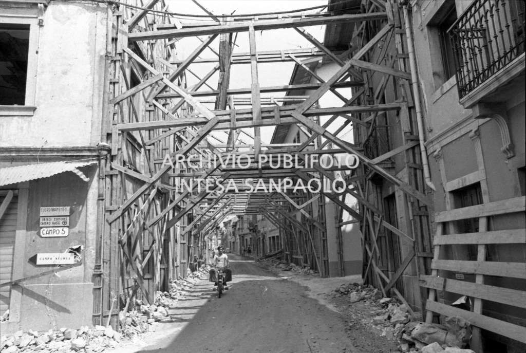 Strutture di sostegno per le facciate degli edifici in una delle località del Friuli colpite dal terremoto, sono visibili alcuni cartelli che segnalano la direzione per raggiungere il comune, la scuola e i campi