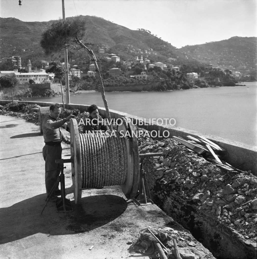 Operai della SIRTI (Società Italiana Reti Telefoniche Interurbane) posano cavi nei pressi di Recco; visibile sullo sfondo la chiesa di San Francesco