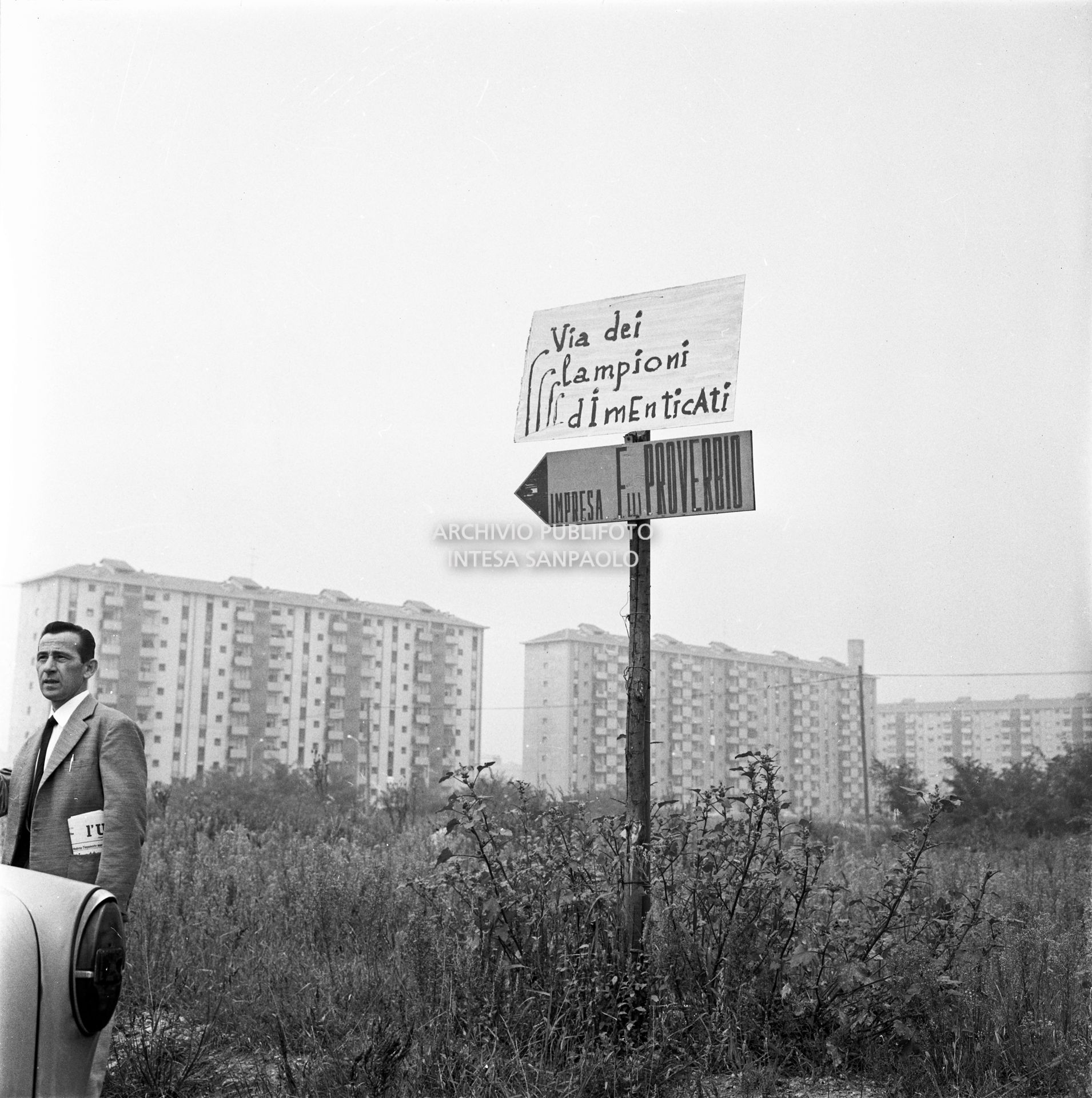 Cartello di protesta per la mancanza di lampioni nel nuovo quartiere Gallaratese, visibile un uomo e un cartello dell'Impresa Fratelli Proverbio