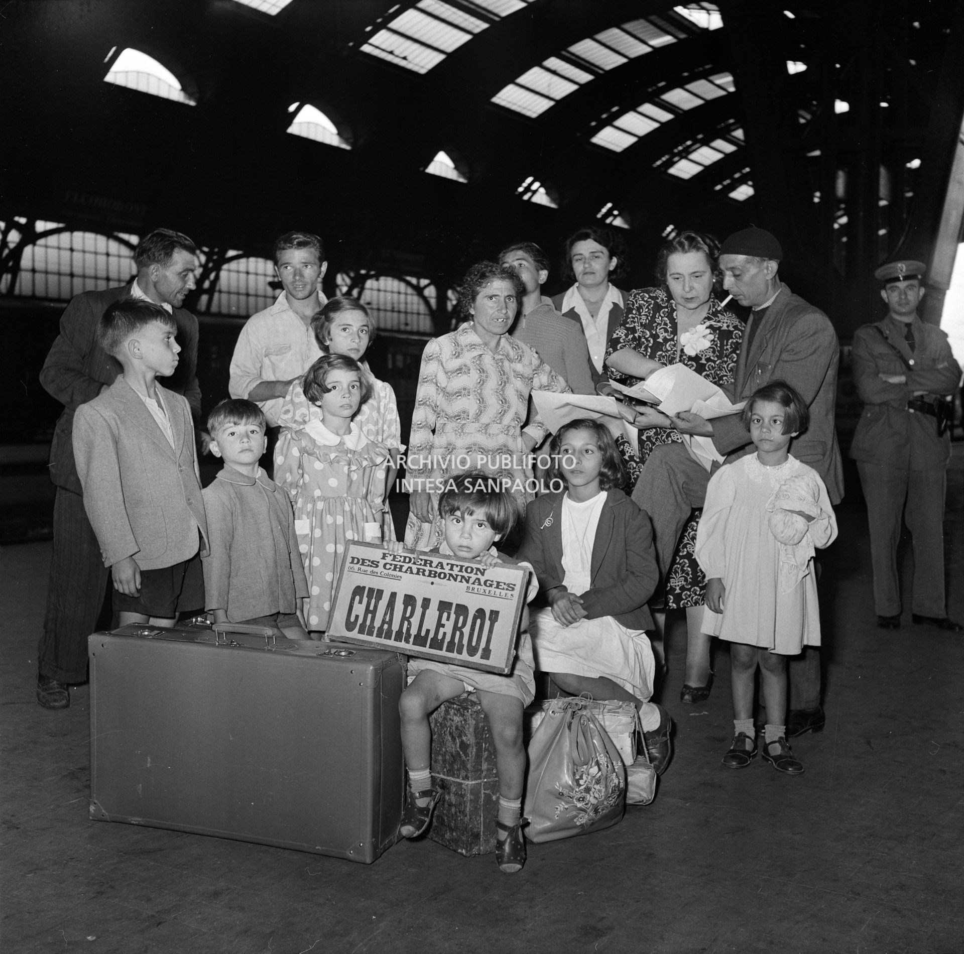 Un gruppo di emigranti in partenza per Charleroi in Belgio, dalla Stazione Centrale di Milano. Uno di loro tiene in mano il cartello: "Federation des charbonnages 66, rue des Colonies, Bruxelles. Campine"