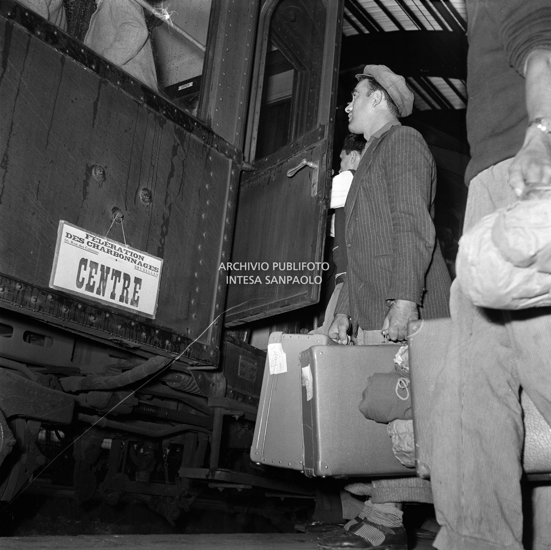 Emigranti in salita su un treno, alla Stazione Centrale di Milano, che li porterà in Belgio. Sul treno il cartello: "Federation des charbonnages 66, rue des Colonies, Bruxelles. Centre"