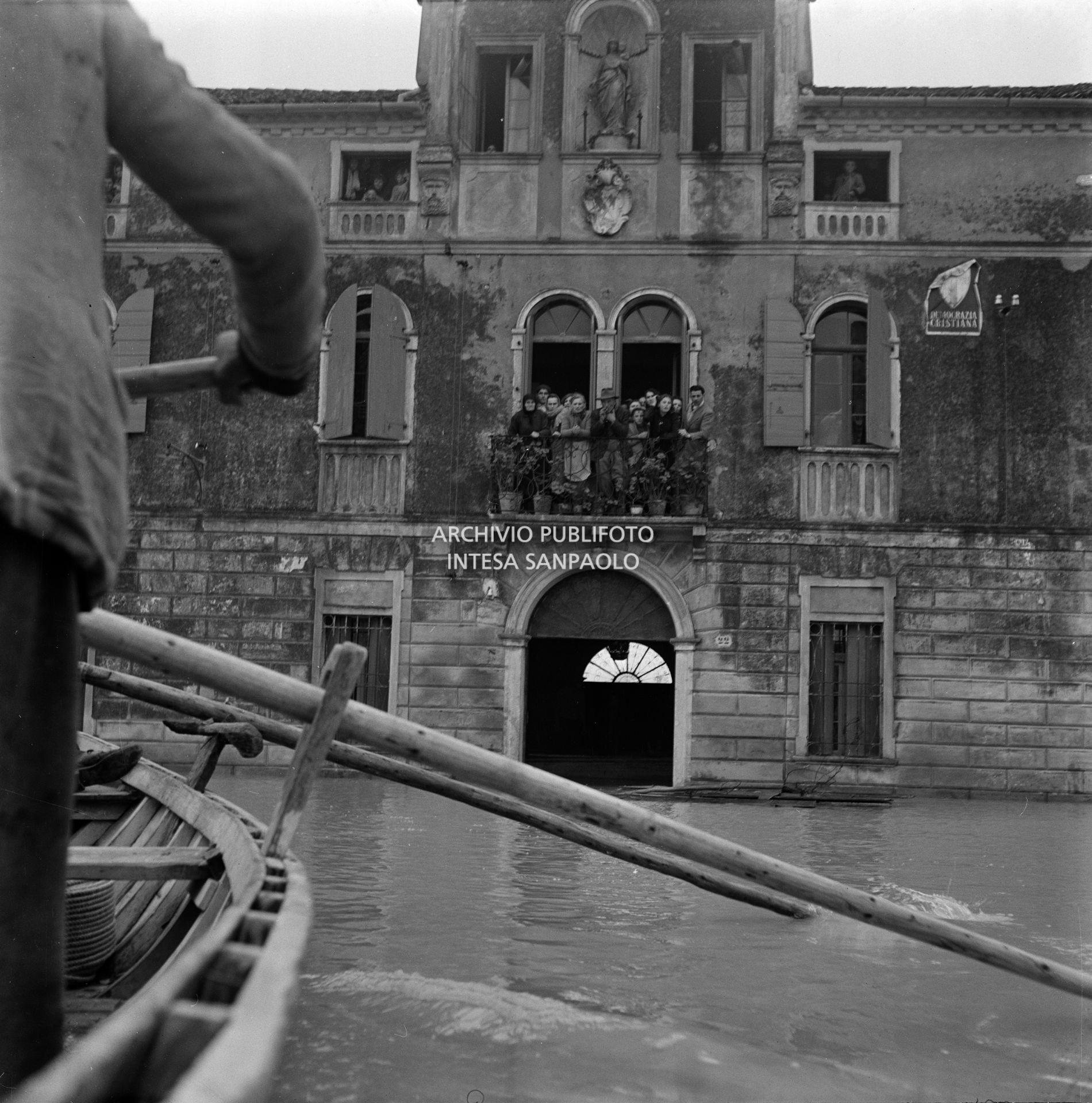 Persone affacciate alle finestre di un edificio parzialmente sommerso dall'acqua durante l'alluvione del Polesine