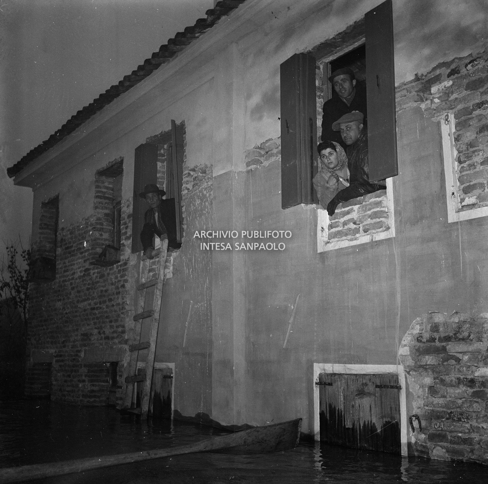 Persone affacciate alle finestre di un edificio parzialmente sommerso dall'acqua durante l'alluvione del Polesine
