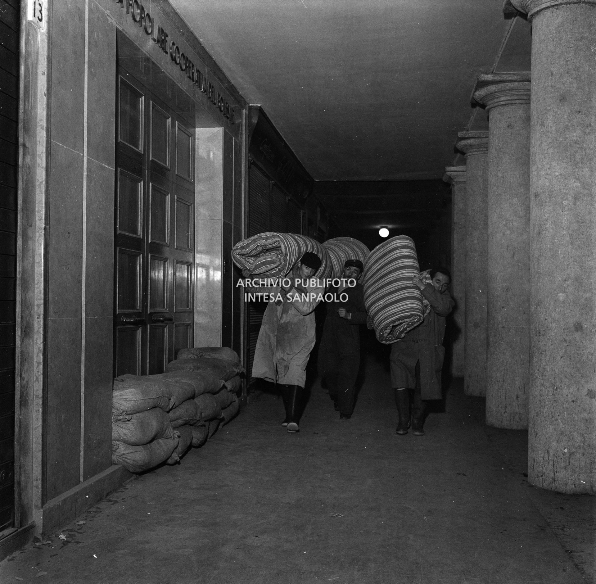 Tre uomini trasportano a spalla altrettanti materassi nei giorni dell'alluvione del Polesine