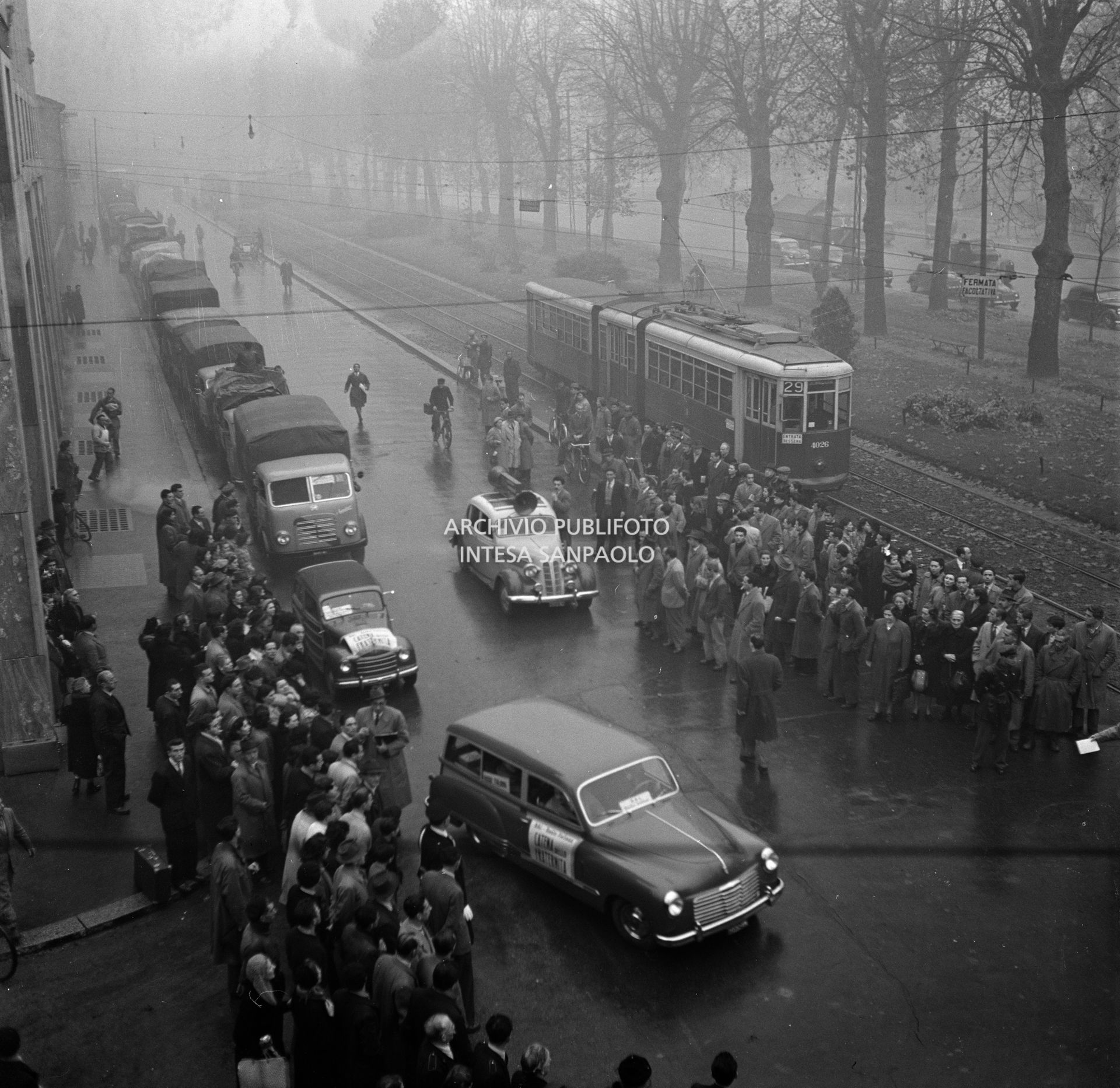 Passanti e curiosi assistono alla partenza della colonna della "Catena della Fraternità", trasmissione radiofonica della RAI con la quale si promosse l'appello alla solidarietà agli alluvionati del Polesine, dalla sede RAI di corso Sempione a Milano.