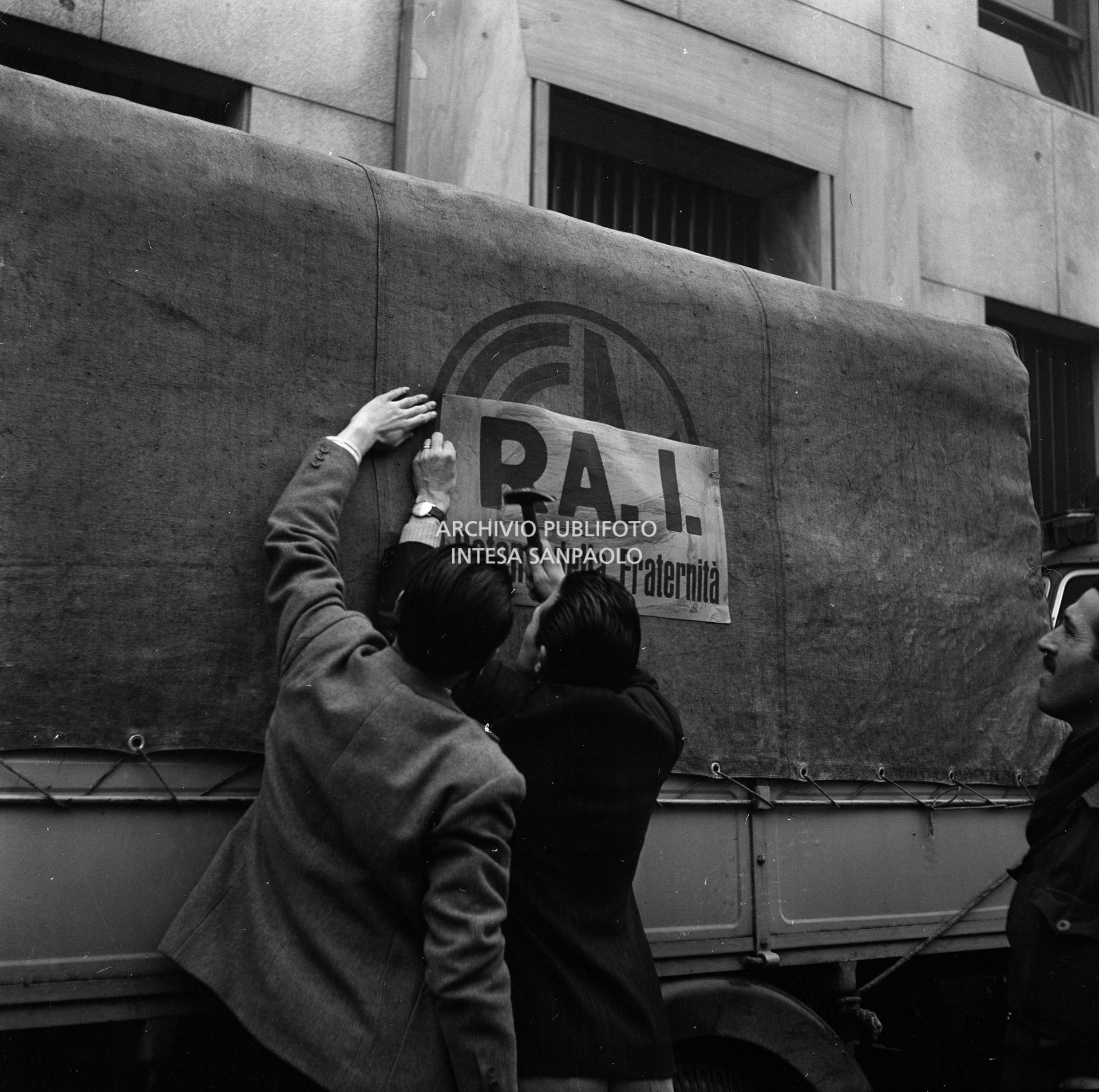 Affissione del cartello "RAI Catena della fraternità" a un autocarro della colonna della trasmissione radiofonica della RAI con la quale si promosse l'appello alla solidarietà agli alluvionati del Polesine, dalla sede RAI di corso Sempione a Milano