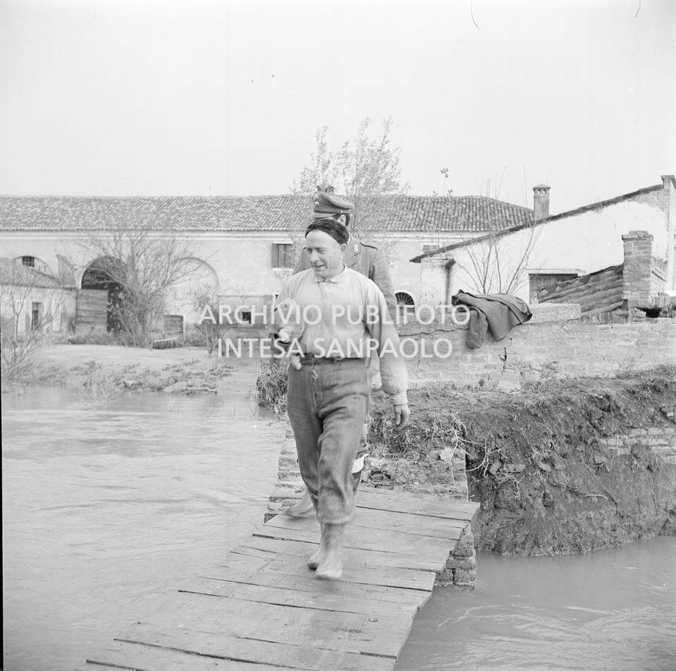 Un uomo, con un coniglio in braccio, e un militare percorrono una passatoia di fortuna, a Sant'Apollinare, una frazione di Rovigo, nei giorni dell'alluvione del Polesine