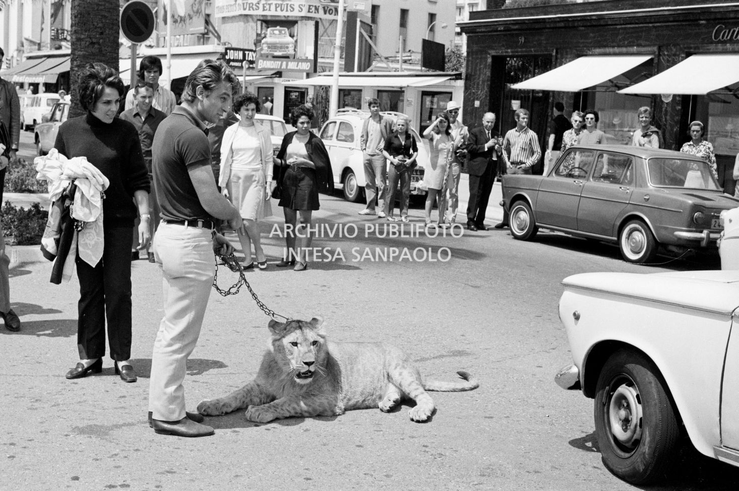 Un uomo in posa con una giovane leonessa alla catena, per le vie di Cannes, tra i passanti incuriositi