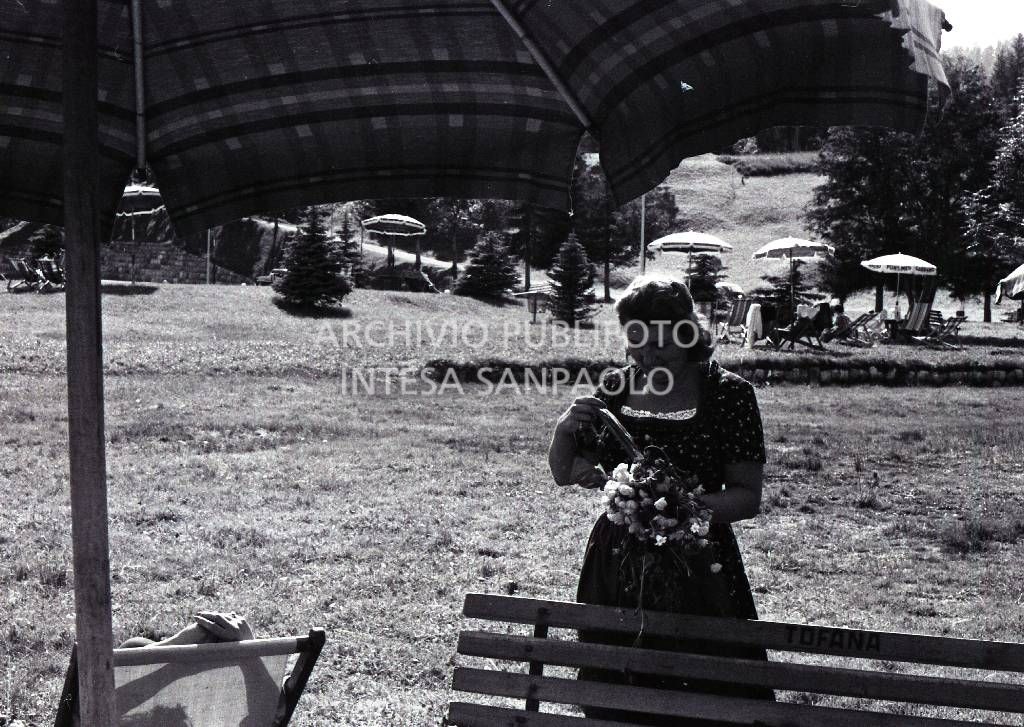 Donna con un mazzo di fiori in un prato a Cortina d'Ampezzo ; sullo sfondo ombrelloni e sdraio<br>706765/90