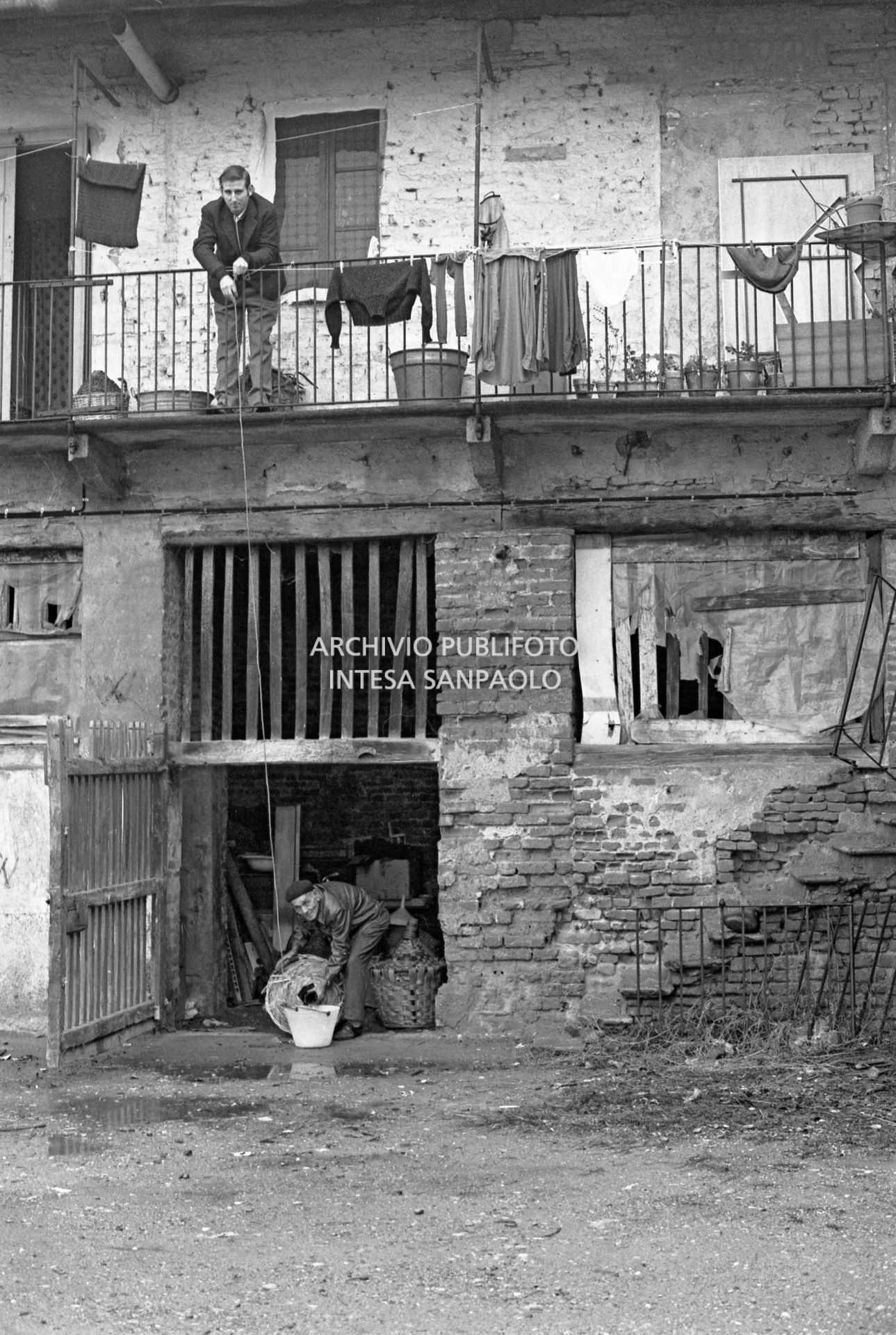 Due uomini nel cortile di una ex cascina agricola del quartiere Gratosoglio a Milano riempiono un secchio da una damigiana