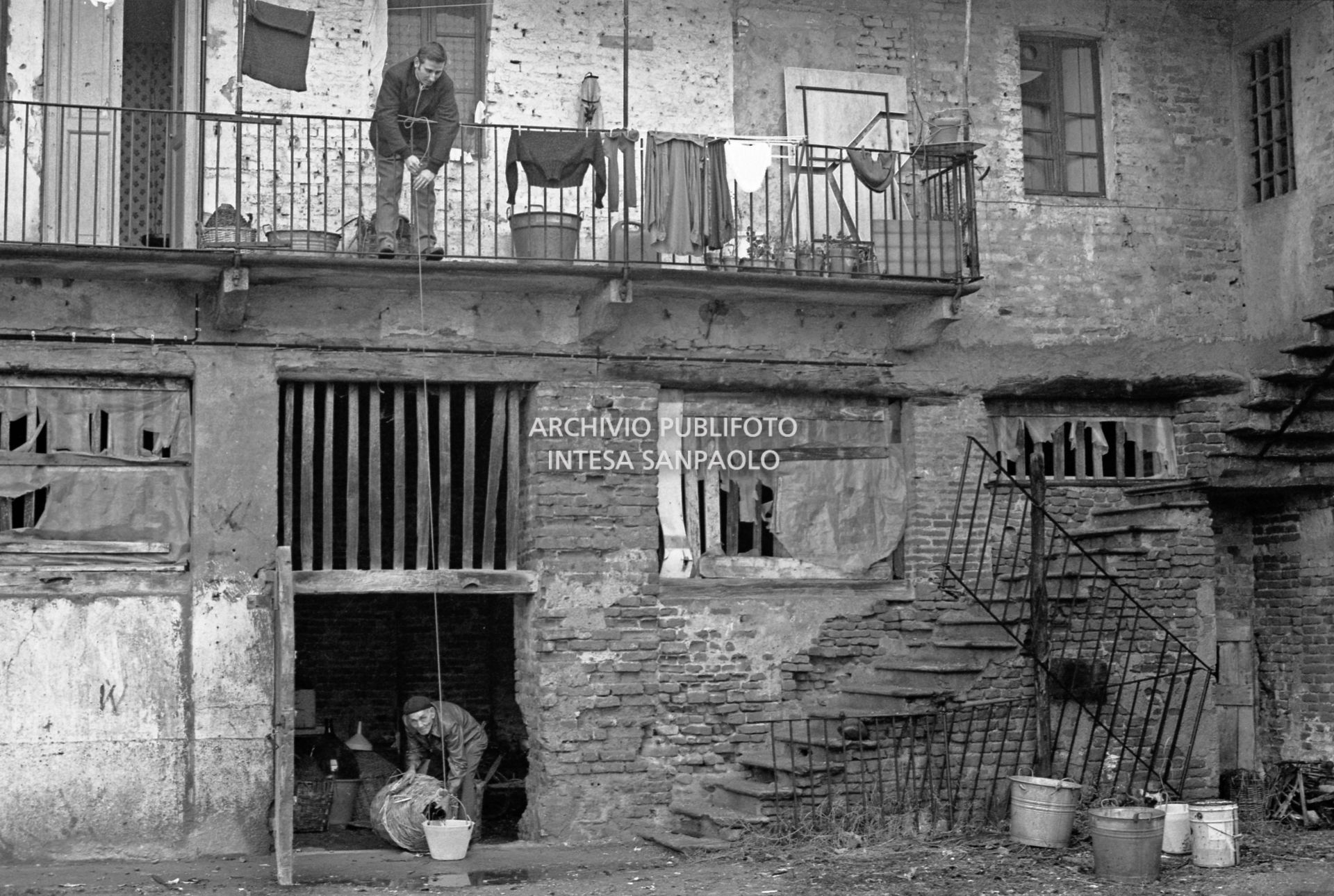Due uomini nel cortile di una ex cascina agricola del quartiere Gratosoglio a Milano riempiono un secchio da una damigiana