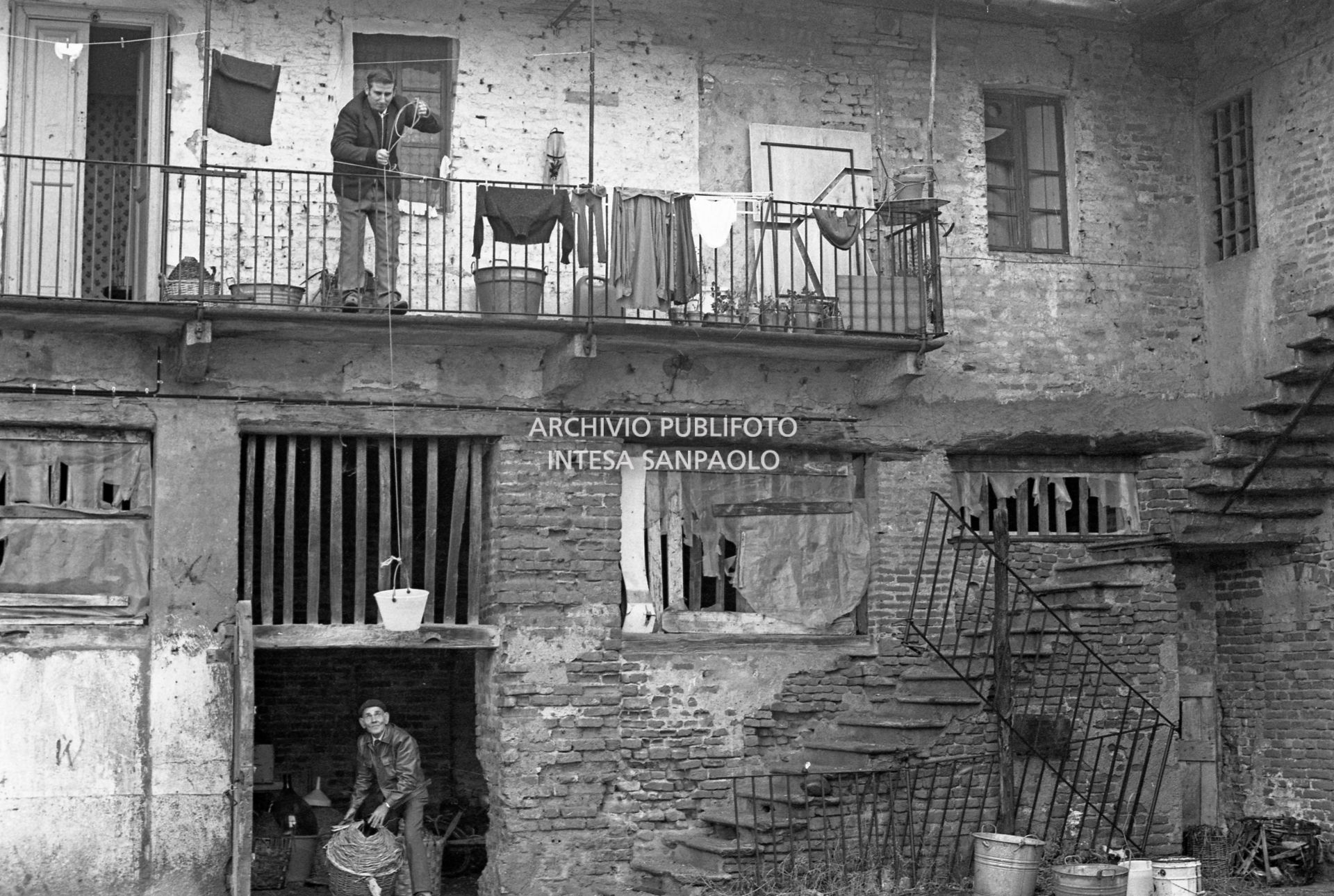 Due uomini nel cortile di una ex cascina agricola del quartiere Gratosoglio a Milano riempiono un secchio da una damigiana