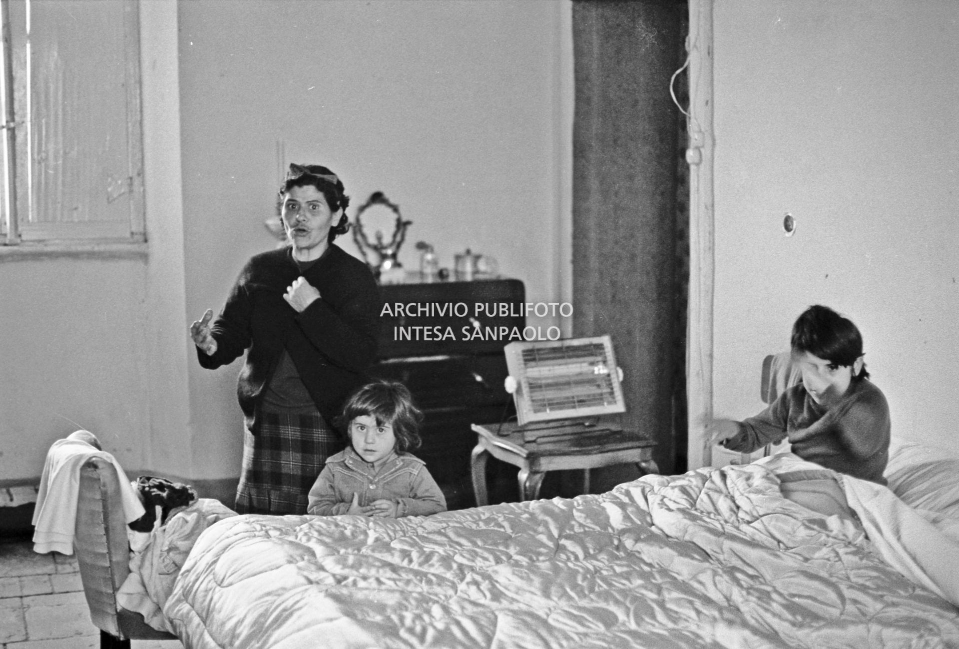 Una donna con la figlia a letto e un altro figlio ritratti in camera da letto di una ex cascina agricola del quartiere Gratosoglio a Milano