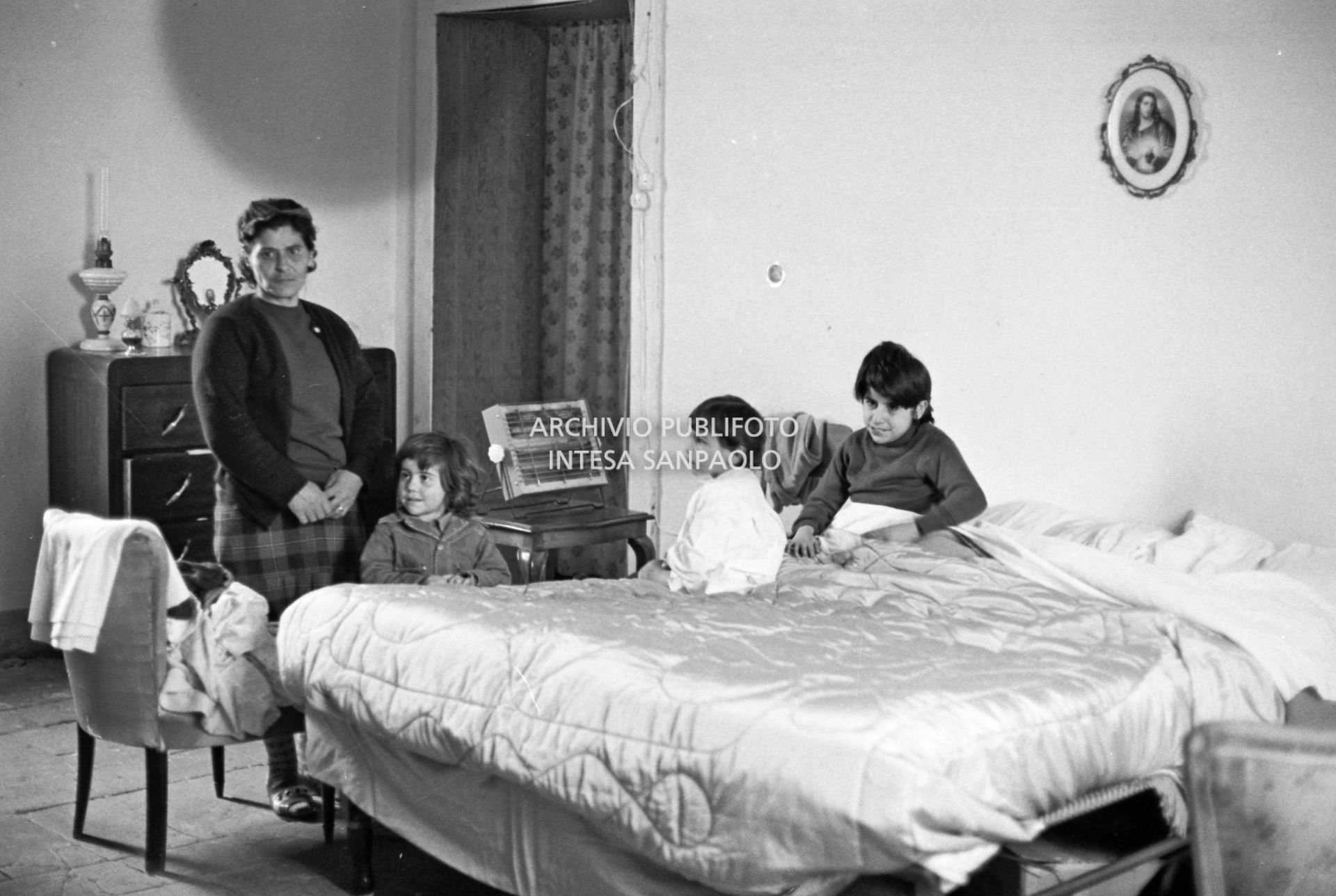 Una donna con la figlia a letto e un altro figlio ritratti in camera da letto di una ex cascina agricola del quartiere Gratosoglio a Milano