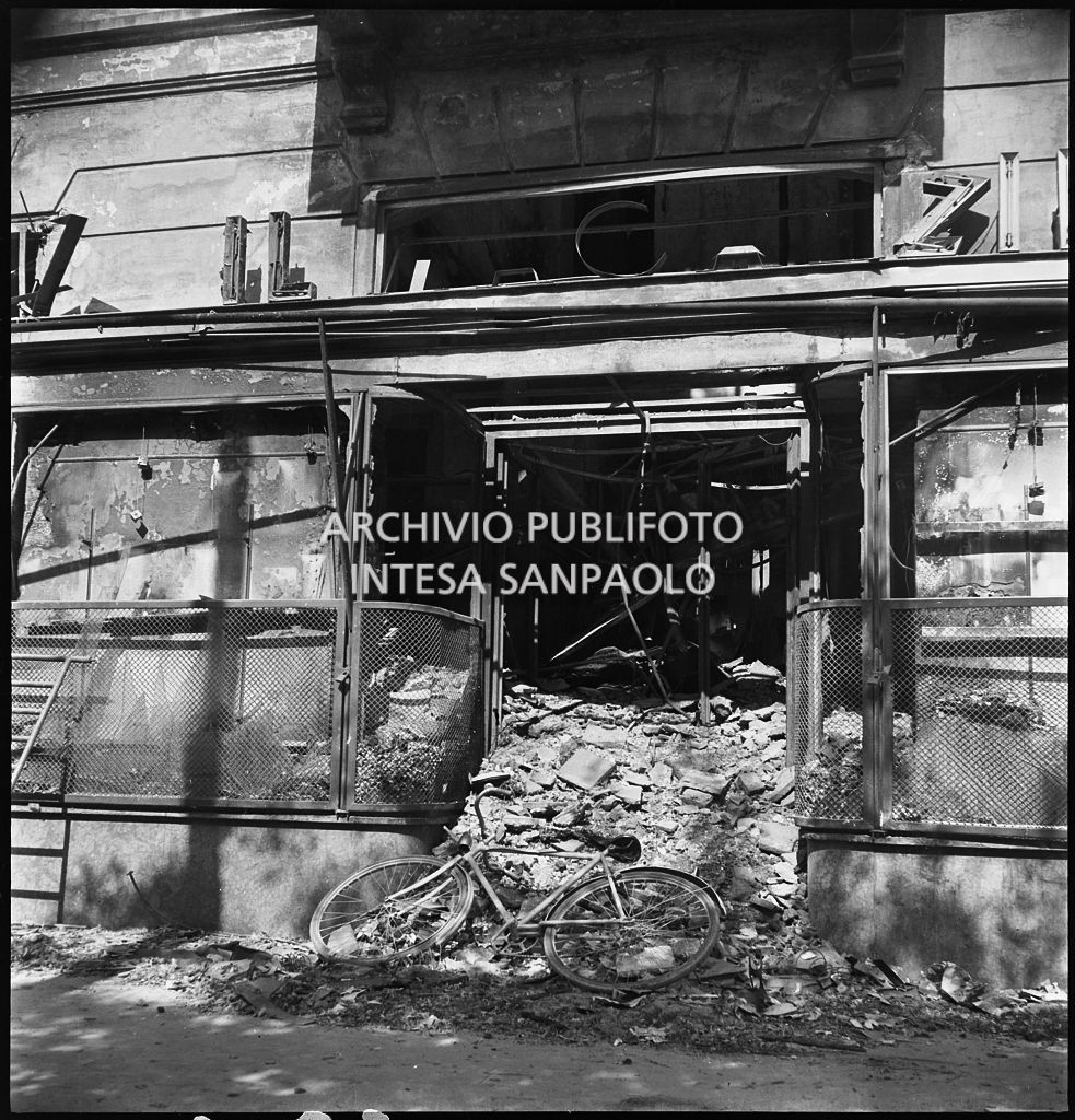 Ingresso del magazzino Upim, in piazzale Antonio Baiamonti, a Milano, distrutto dai bombardamenti e ingombro di macerie sulle quali è appoggiata una bicicletta