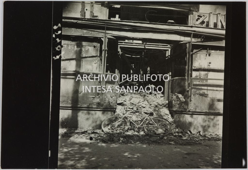 Ingresso del magazzino Upim, in piazzale Antonio Baiamonti, a Milano, distrutto dai bombardamenti e ingombro di macerie sulle quali è appoggiata una bicicletta