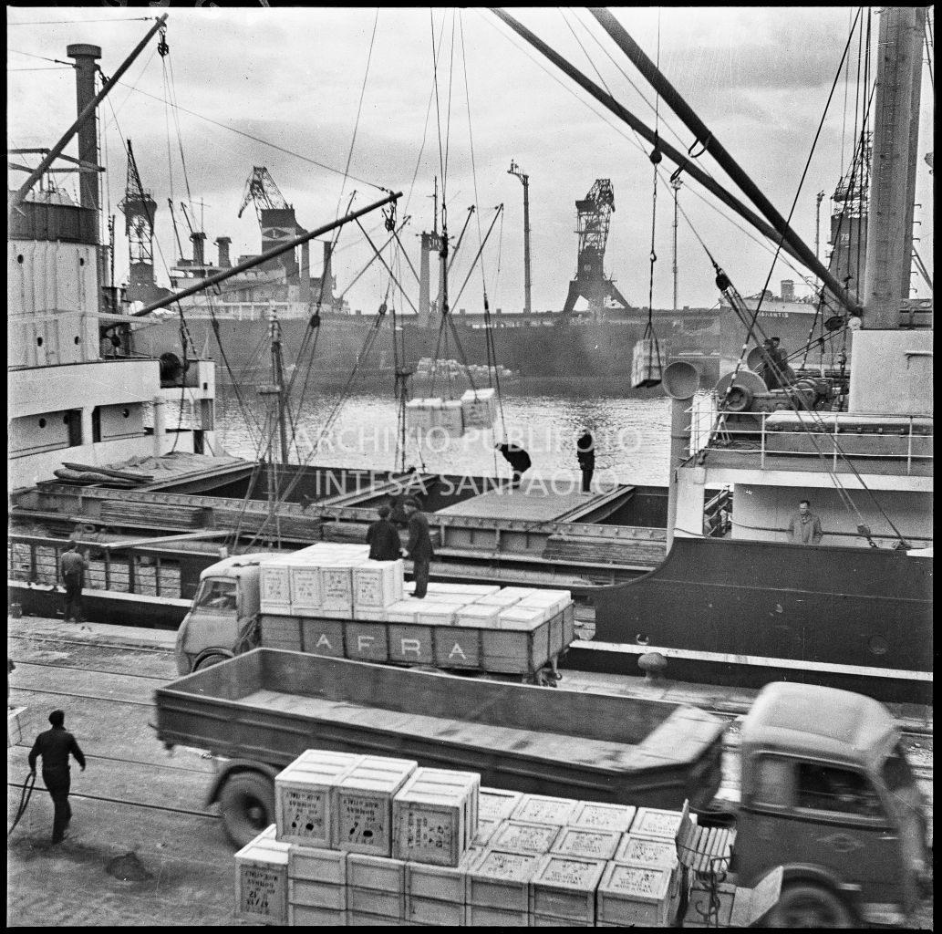 Carico per l'esportazione su una nave mercantile attraccata al porto di Genova. Sulla banchina due autocarri, uno dei quali con la scritta: "AFRA".<br>23265