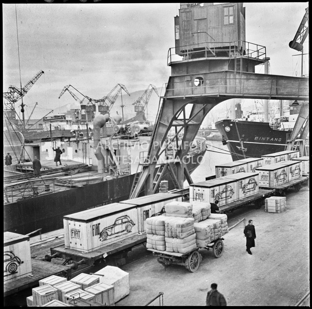 Treno merci, carico di automobili Fiat 1500 per l'esportazione, sulla banchina al porto di Genova;a fianco due carri carichi di merce<br>23268