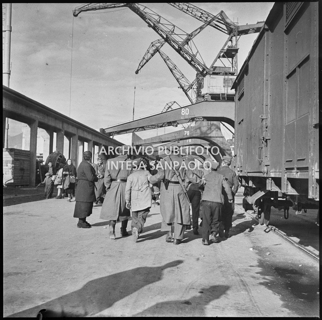 Poliziotti di pattuglia al porto di Genova hanno fermato alcuni ragazzini che tengono per la giacca: sulla destra carri merci, sullo sfondo gru portuali.<br>23279