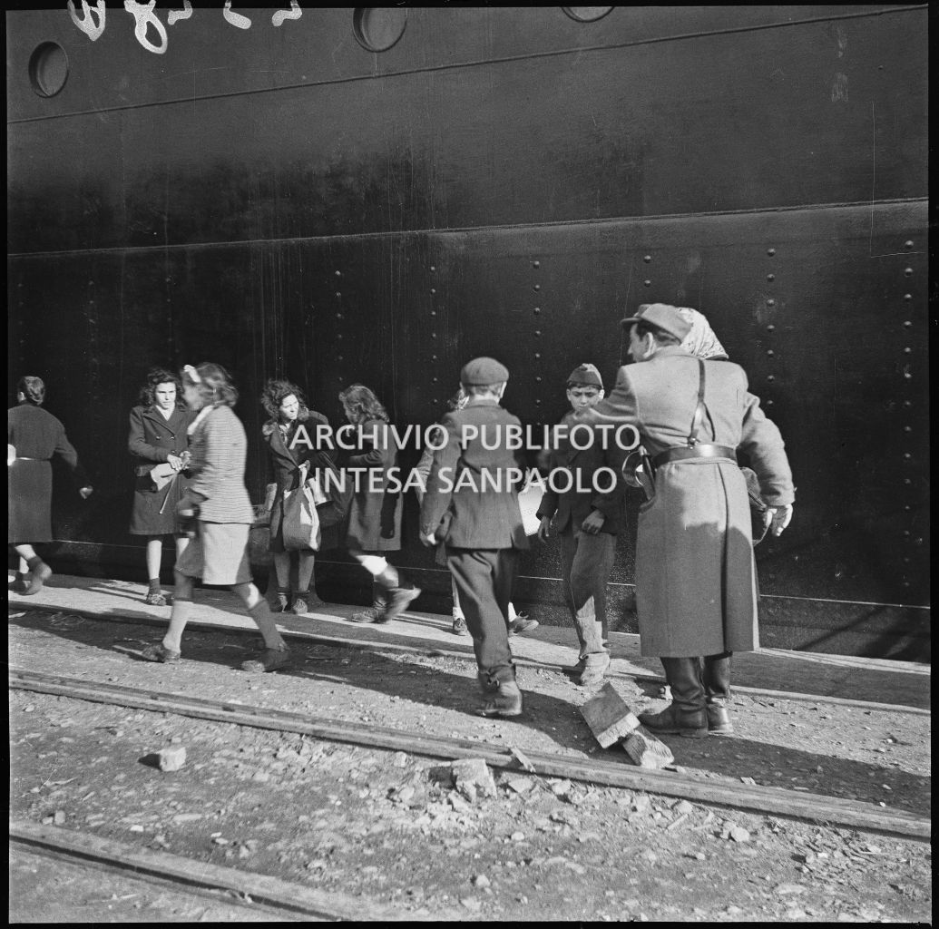 Un poliziotto di pattuglia al porto di Genova si rivolge ad alcuni ragazzini. Sullo sfondo la fiancata di una nave<br>23280