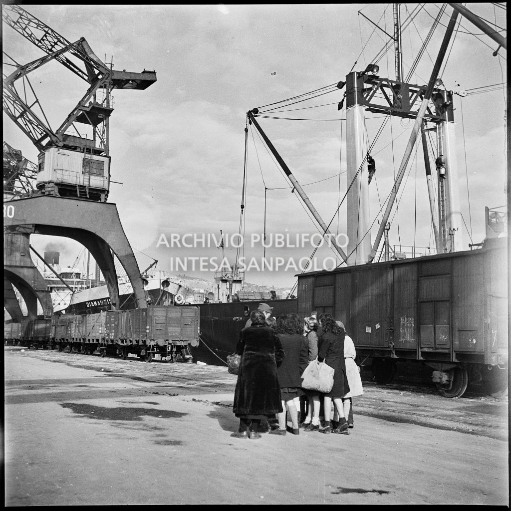 Capannello di persone intorno a un agente di polizia di pattuglia al porto di Genova: sulla destra un treno merci<br>23283