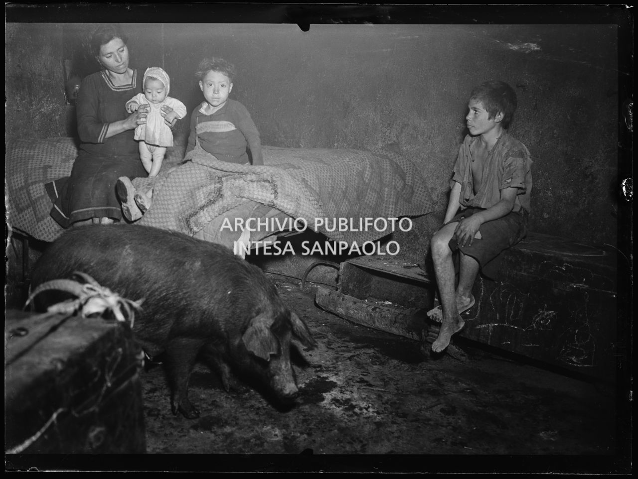 Africo, interno con due bambini, una donna che tiene in braccio un neonato, un maiale e una capra