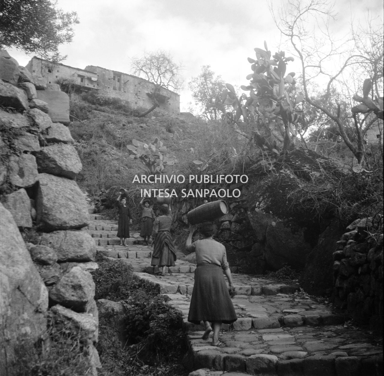 Africo, donne e ragazzine trasportano botti di legno e giare sulla testa lungo una scalinata, nella campagna sottostante il paese