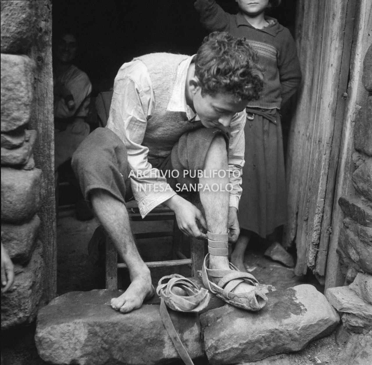 Africo, un ragazzo calza delle cioce, calzature tradizionali, seduto sulla soglia di casa