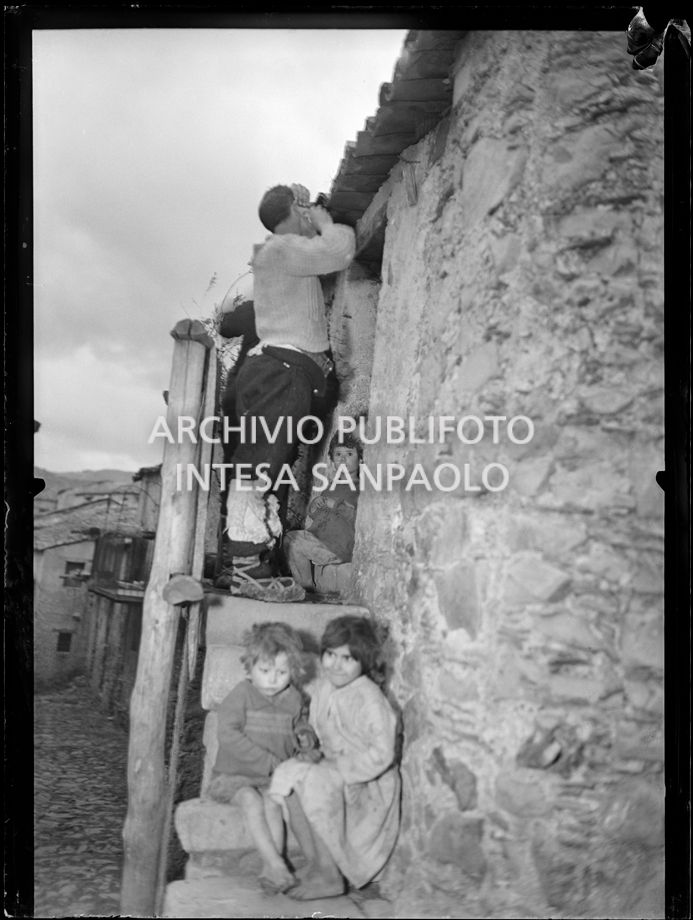 Africo, un uomo si fa la barba in cima alla scala all'esterno di casa; intorno a lui molti bambini