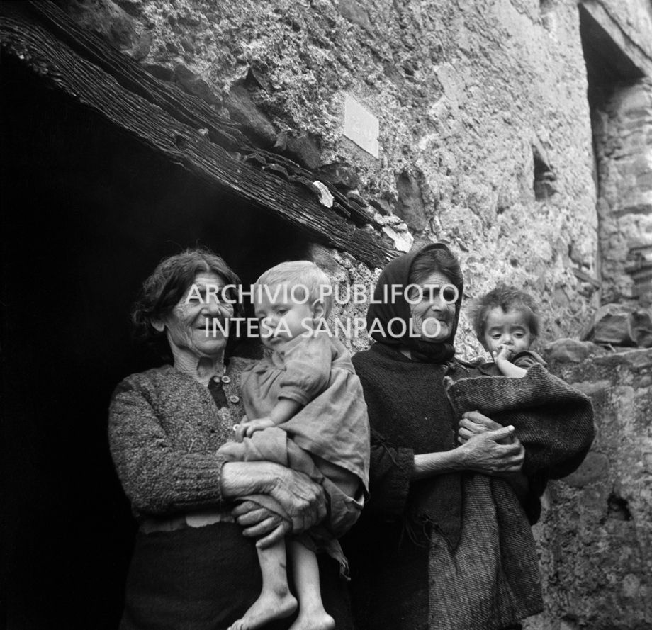 Africo, ritratto di due donne con in braccio due bambini sulla soglia di una casa