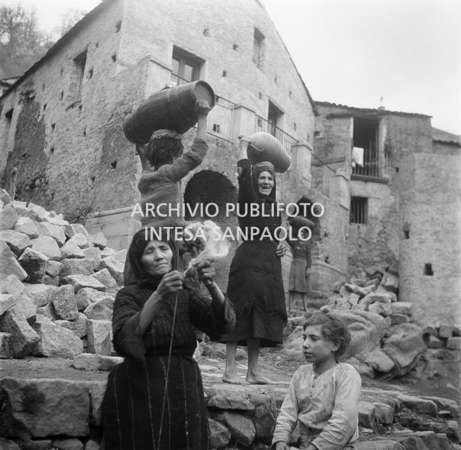 Africo, donne scalze ritratte in paese, con sulla testa botti di legno e giare o un fuso di filato in mano