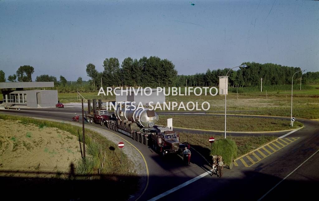 Un contadino con un carro agricolo nei pressi di un uscita autostradale, visibile un convoglio speciale fermo all'uscita