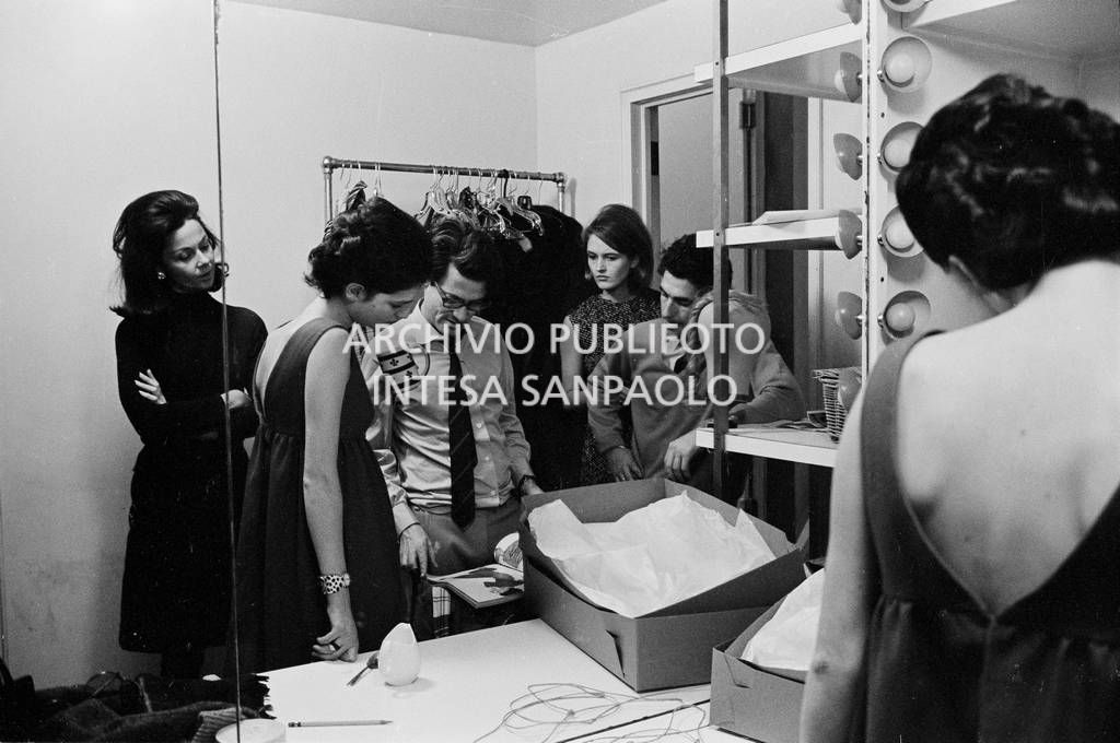 Benedetta Barzini, Richard Avedon e alcuni collaboratori guardano una rivista in camerino<br>727793/1