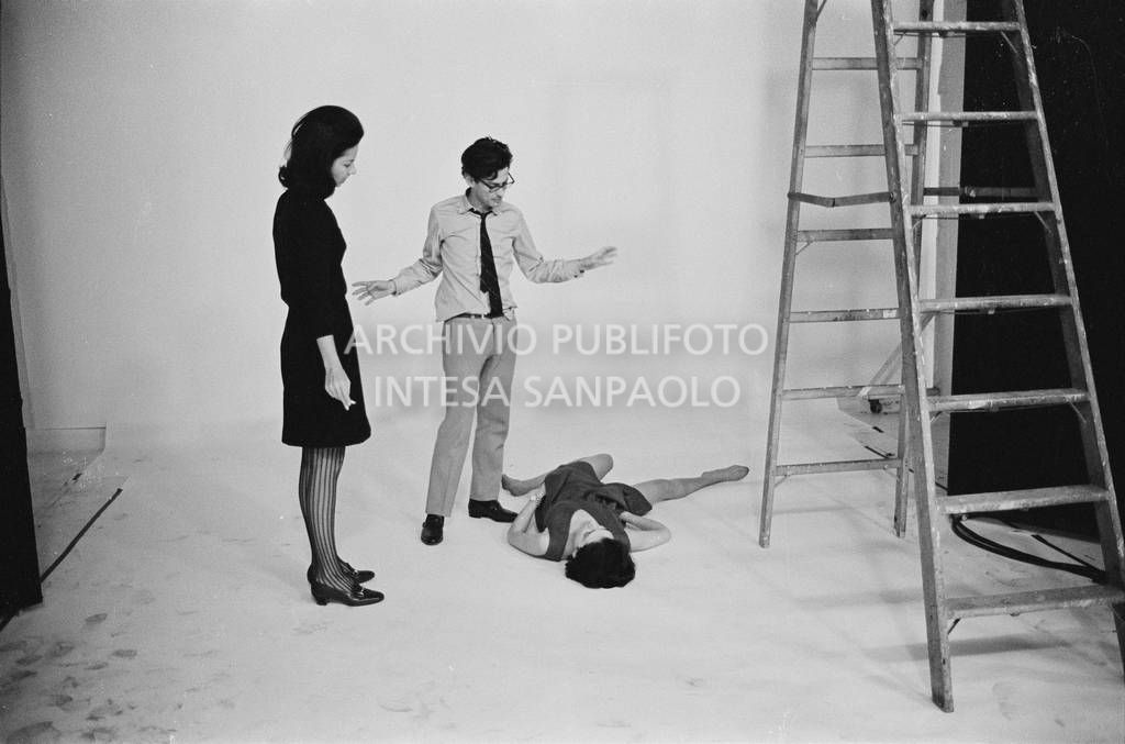 Set fotografico: Benedetta Barzini sdraiata in posa, Richard Avedon la dirige con una collaboratrice<br>727793/23