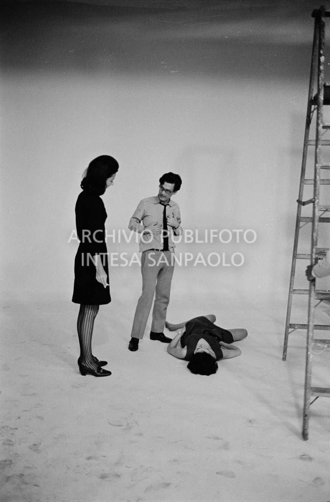 Set fotografico: Benedetta Barzini sdraiata in posa, Richard Avedon la dirige con una collaboratrice<br>727793/24