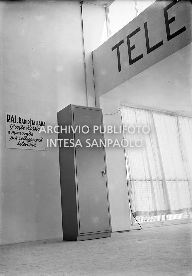 Un armadio General Electric alla Fiera di Milano; alla parete è affisso un cartello esplicativo con la scritta: "RAI Radio Italiana. Ponte radio a microonde per collegamenti televisivi"