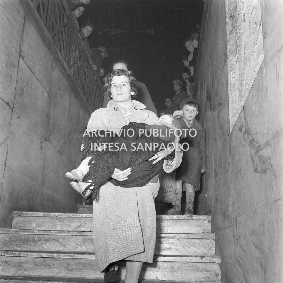 Sfollati dal Polesine appena arrivati alla Stazione Centrale di Milano: in primo piano una donna con una bambina addormentata in braccio mentre scende le scale