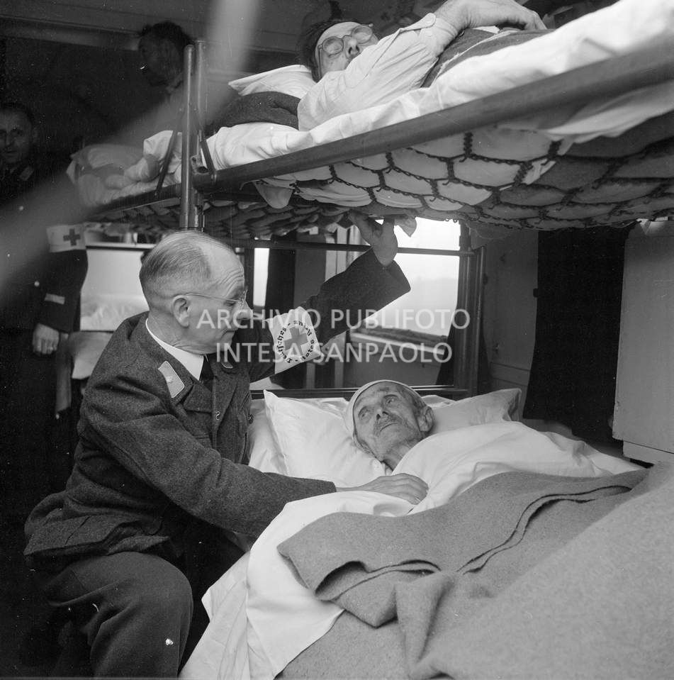 Un medico della Croce Rossa Tedesca accosciato a fianco a un uomo, alluvionato del Polesine, all'interno di un treno ospedale, inviato in soccorso agli alluvionati del Polesine, a Pontelagoscuro, frazione di Ferrara<br>113902