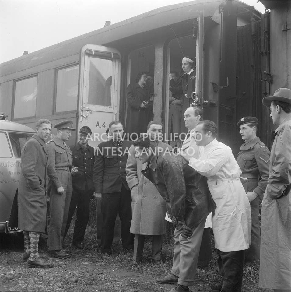 Militari inglesi e tedeschi all'esterno di un treno ospedale inviato in soccorso agli alluvionati del Polesine, a Pontelagoscuro, frazione di Ferrara. un medico scrive su un foglio appoggiandosi alla schiena di un uomo<br>113911