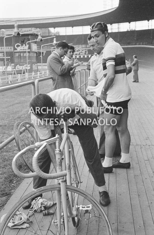 Giuseppe De Grandi, detto Pinella, esegue gli ultimi controlli alla bicicletta che ha preparato per Roger Rivière, alle sua spalle, al velodromo Vigorelli di Milano