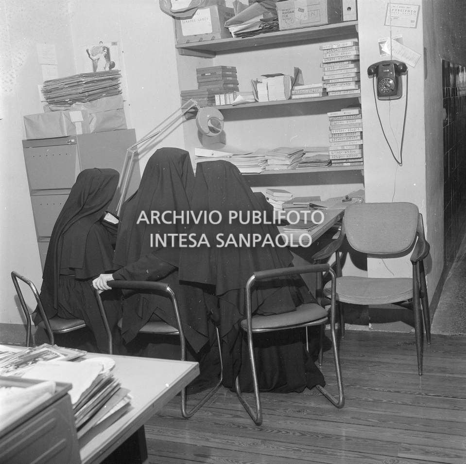 Tre suore, riprese di spalle, sedute a un tavolo dell'agenzia Publifoto