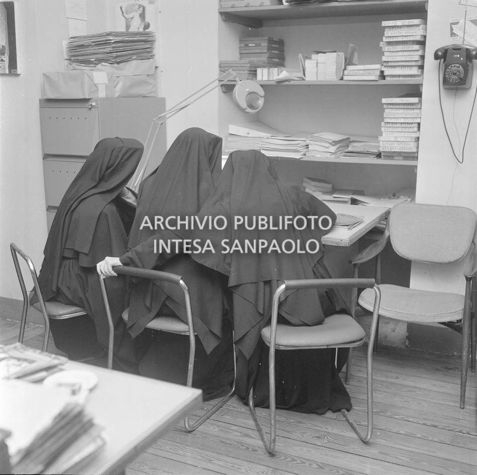Tre suore, riprese di spalle, sedute a un tavolo dell'agenzia Publifoto