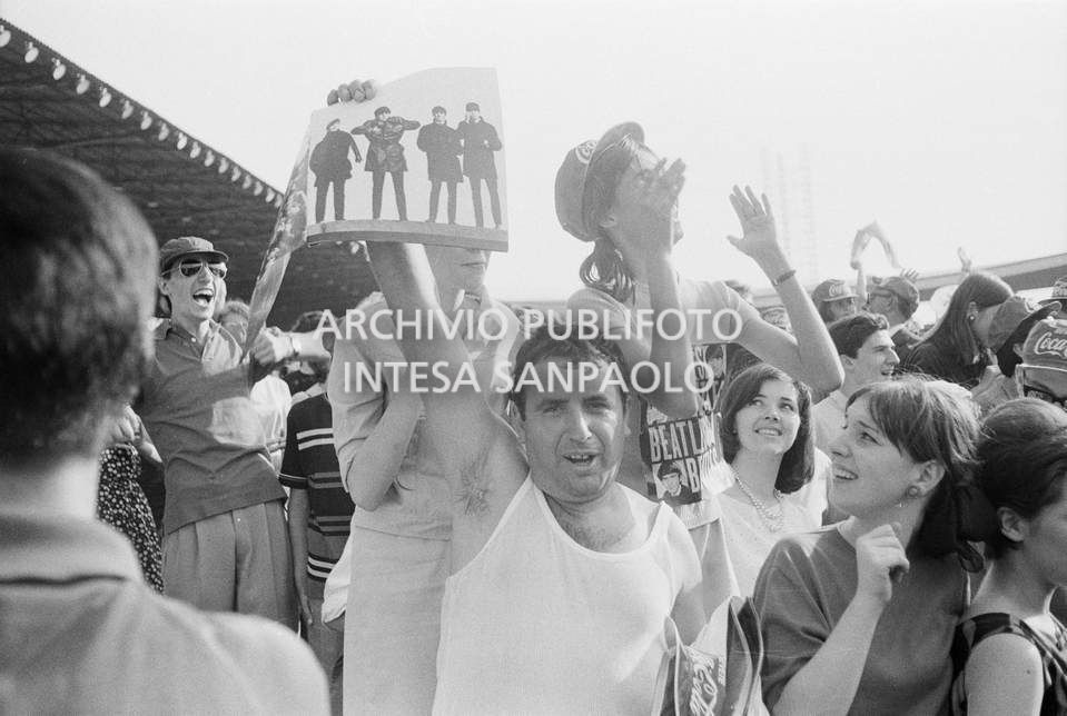 Fan scatenati al concerto pomeridiano dei Beatles al Vigorelli di Milano: un uomo mostra una fotografia della band