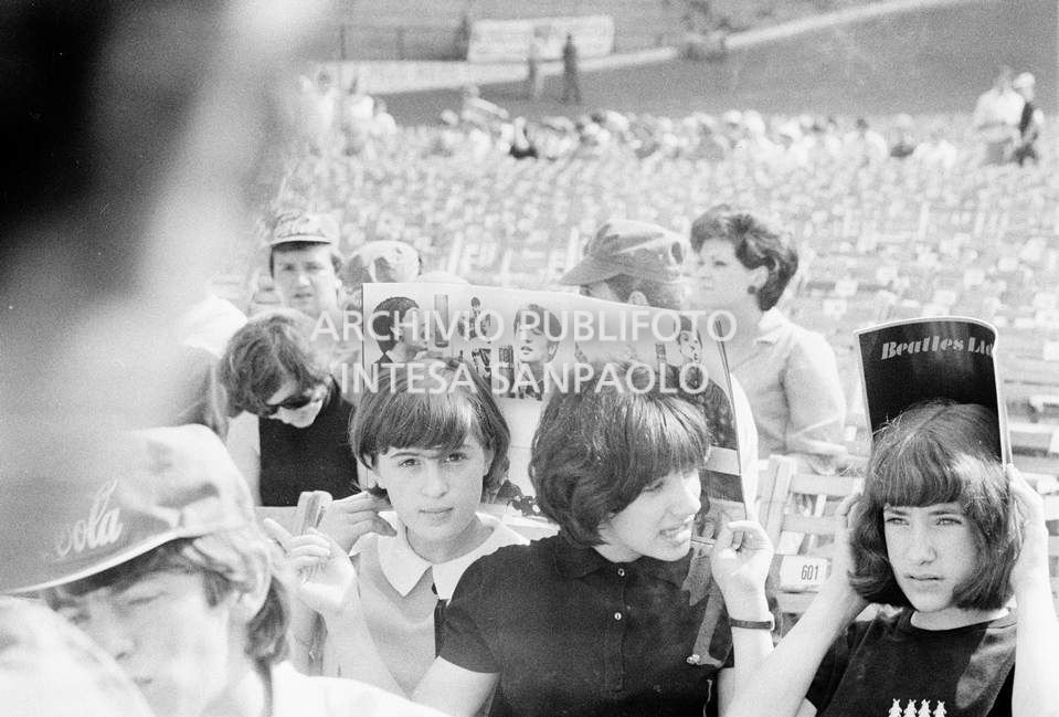 Tre ragazze si riparano dal sole con il programma del concerto dei Beatles, in attesa dell'inizio, al Vigorelli di Milano