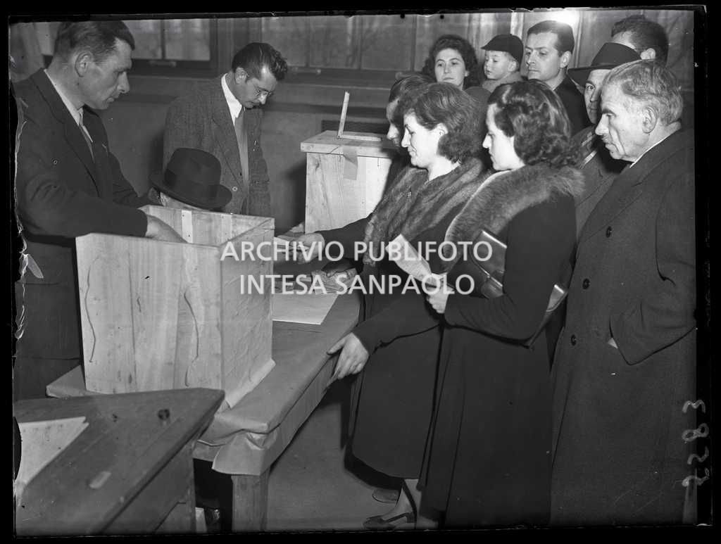 Una donna consegna il certificato elettorale al seggio in occasione delle elezioni comunali nel Saronnese, le prime elezioni con suffragio universale in Italia