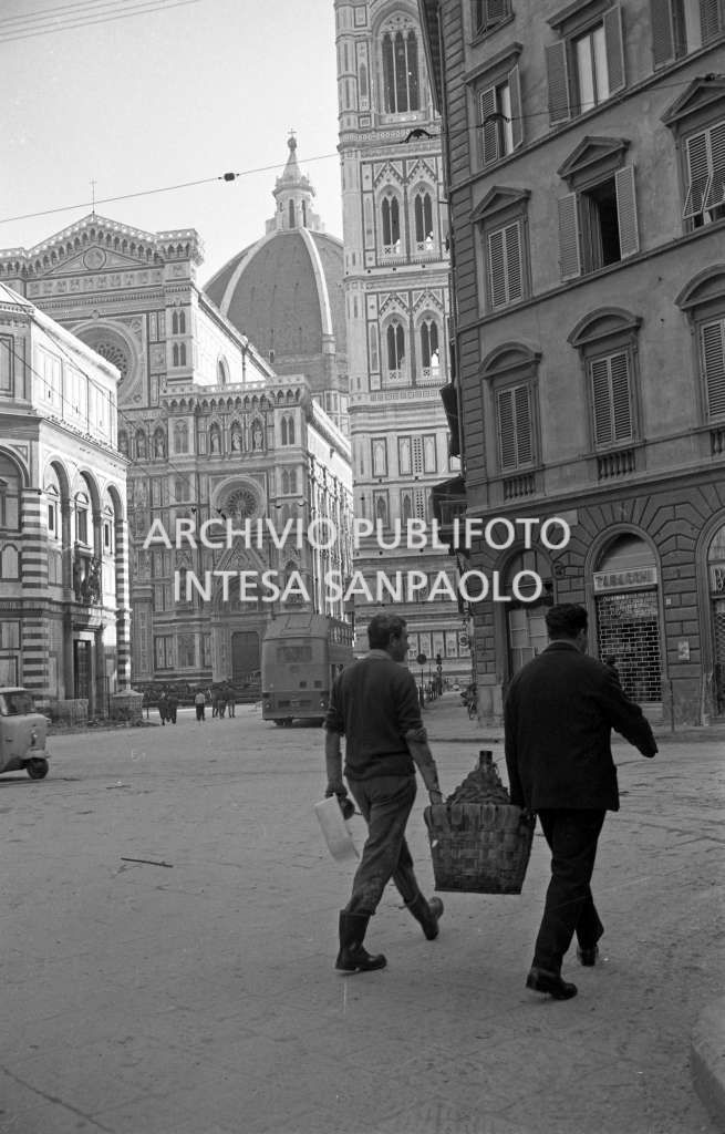 Due uomini trasportano una damigiana per le strade di Firenze nei giorni successivi all'alluvione. Sullo sfondo il Duomo