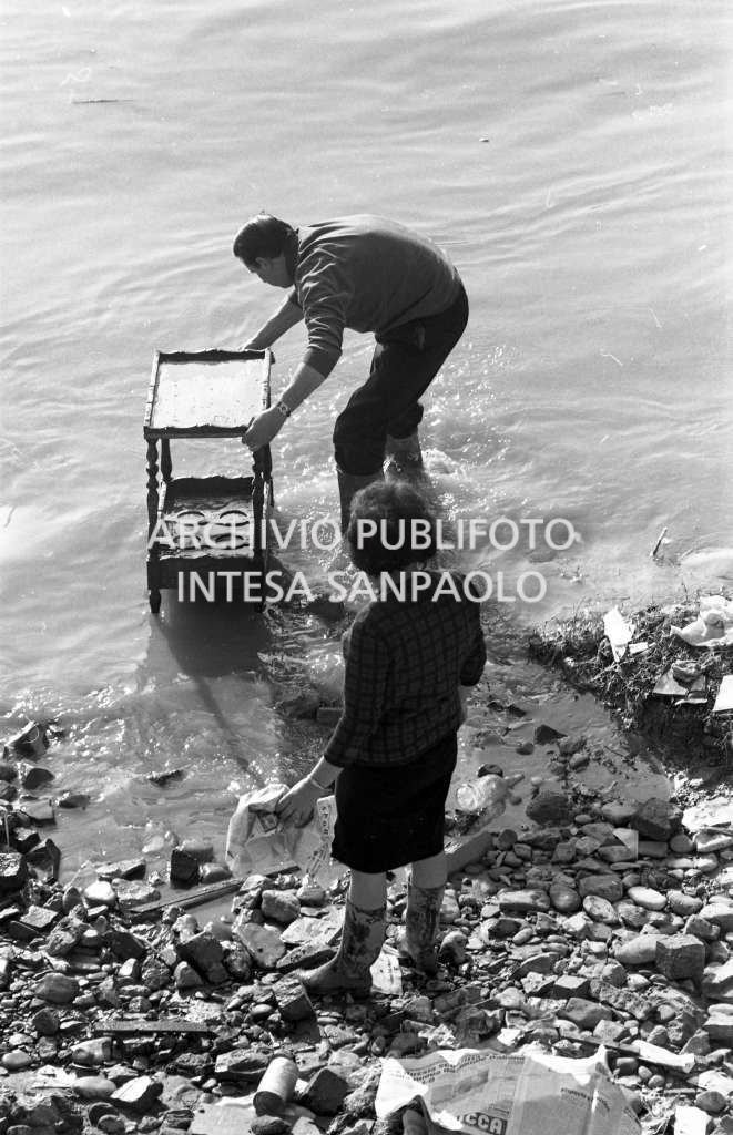 Un uomo e una donna sciacquano un mobile dal fango dell'alluvione di Firenze