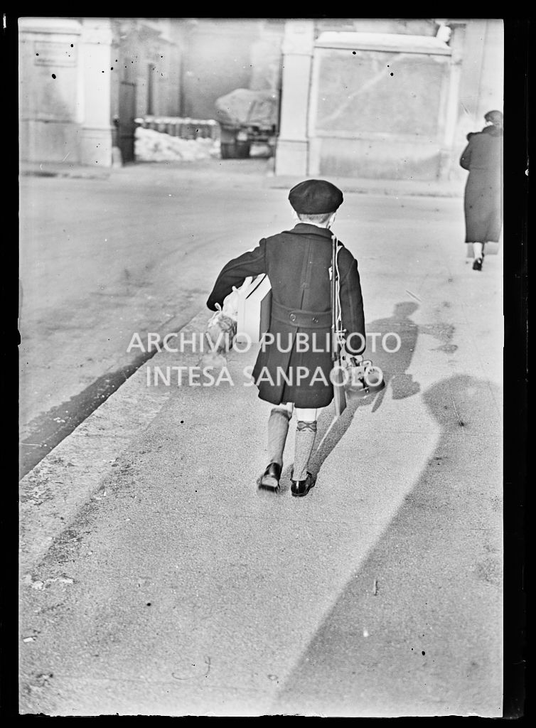 Un bambino, di spalle, trasporta un fucile giocattolo, un violino, una bambola e una scatola